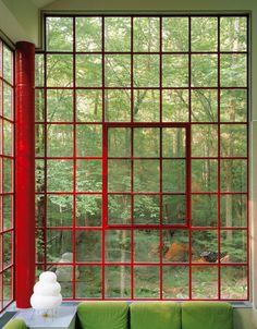 a green couch sitting in front of a window next to a red pillar and table