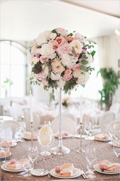 a tall vase filled with pink and white flowers on top of a table covered in silverware