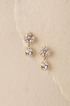 two pairs of earrings on top of a white cloth covered surface, one with crystal stones and the other with gold tone accents