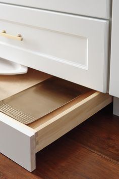 an open drawer in a white kitchen with wood flooring