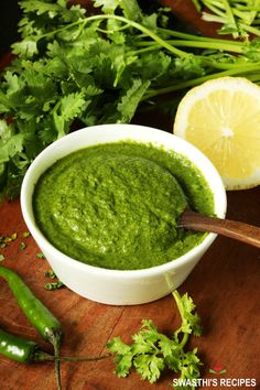 a white bowl filled with green pesto next to sliced lemon and parsley