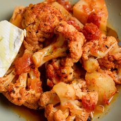 a plate full of cooked cauliflower and potatoes with butter on the side,