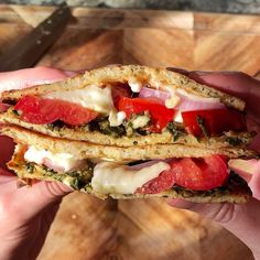 a hand holding a sandwich with tomatoes and cheese