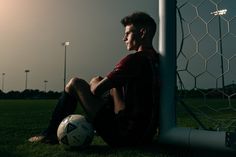 a man sitting on the ground next to a soccer ball in front of a goal