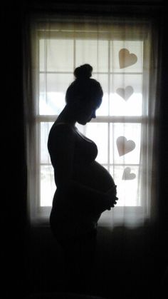 a pregnant woman standing in front of a window with hearts drawn on the windowsill