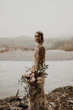 a woman standing in front of a body of water wearing a dress with flowers on it