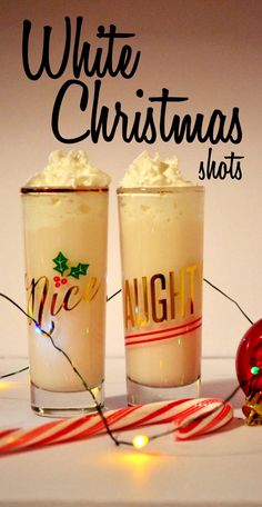 two glasses filled with white christmas shots on top of a table next to candy canes