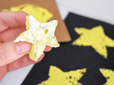 a hand holding a piece of food in front of some yellow and black designs on paper