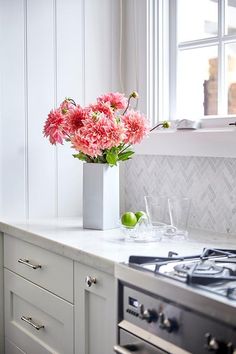 pink flowers are in a vase on the counter top next to an oven and window