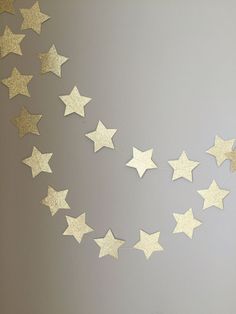 some gold stars are hanging from a string on a gray wall with a clock in the background