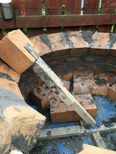 a brick fire pit is being built in the back yard with bricks stacked up around it