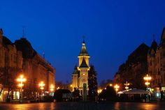 a clock tower lit up at night in the middle of a town square with street lights