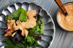 a salad with dressing in a bowl next to a wooden spoon on a table top