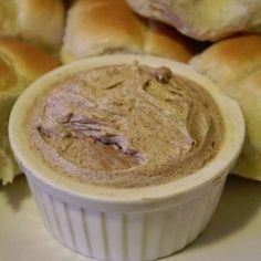 a white bowl filled with peanut butter next to rolls on a plate and another bagel in the background