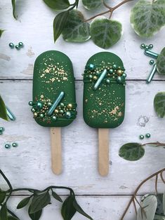 two popsicles with green and gold sprinkles on them sitting next to leaves