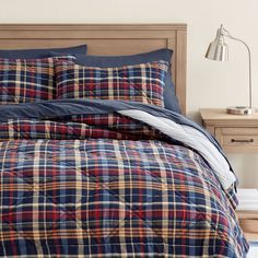 a bed with plaid comforter and pillows on top of it, next to a night stand