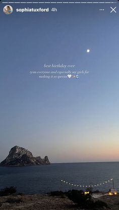 the sky is blue and there are candles on the table near the water with an island in the background