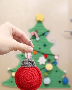 a hand holding a crocheted ornament in front of a christmas tree