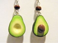 two pieces of avocado are hanging from silver earwires on a white surface