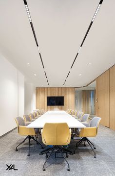 an empty conference room with yellow chairs and a white table in front of a flat screen tv