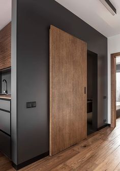 an empty room with wooden floors and black walls, two doors open to the kitchen