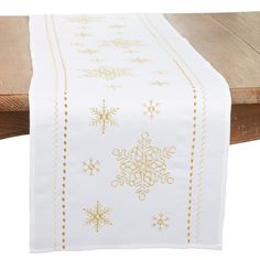 a white table runner with gold snowflakes on it and a wooden bench in the background