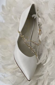 a pair of white shoes with pearls on the side and feathers in the back ground