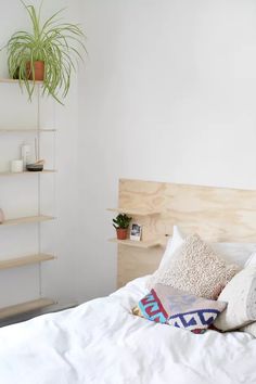 a bed with white sheets and pillows on top of it next to a wooden shelf