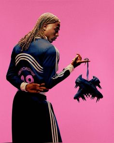 a woman with dreadlocks is holding an object in front of a pink background