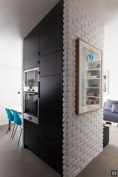 a kitchen with white brick walls and an oven on the wall next to a blue chair