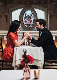 a man and woman sitting at a table in front of each other, holding hands