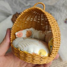 a hand holding a small basket with a pillow inside