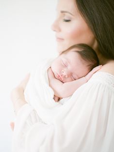 a woman holding a sleeping baby wrapped in a white blanket with her arms around her head