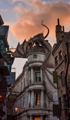 a dragon statue on top of a building in the middle of a city at sunset