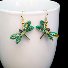 pair of green dragonfly earrings sitting on top of a white cup in front of a black background