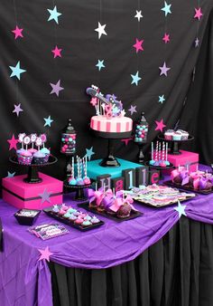 a table topped with lots of cakes and desserts on top of purple cloth covered tables