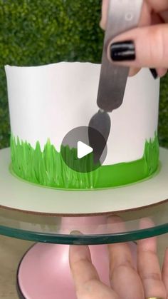 someone is cutting into a cake with green grass on the bottom and white frosting