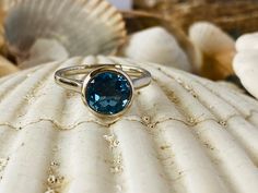 This bezel ring contains a 2.00 ct. genuine London blue topaz. The center stone measures 8mm. The ring is available in sterling silver, and 14k white, yellow or rose gold. The mounting is a modern, elegant setting with a high polish finish. Please send me a message if you need a size not listed. This ring can also be customized with any color center stone. All items are handmade by me in my shop in Woodbridge, NJ. Please message me with any questions. Shipping within the United States is complim Blue Bezel Set Round Cut Birthstone Ring, Blue Topaz Ring With Bezel Setting For Promise, Blue Topaz Ring With Round Cut Bezel Setting, Blue Topaz Ring With Bezel Setting, Blue Topaz Rings With Bezel Setting, Bezel Set Topaz Ring In Fine Jewelry Style, Blue Birthstone Ring With Bezel Setting, Blue Topaz Ring With Round Cut And Tension Setting, Blue Bezel Set Round Stone Ring