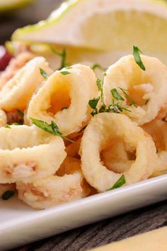 some onion rings are on a plate with lemon wedges and garnishes