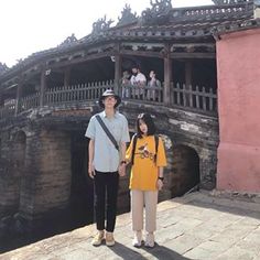 a man and woman standing next to each other in front of a bridge with people on it