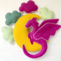 a felt dragon sitting on top of a yellow and pink circle with hearts around it