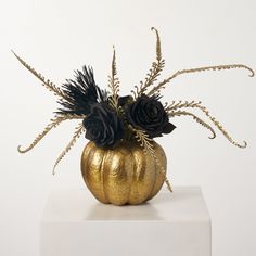 a gold vase filled with black flowers on top of a white table