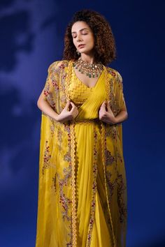 Yellow cape with all over cape with all over vintage pattern, multi color thread embroidery and chevron cut work border. Paired with pre-draped saree with pleated draped details attached pallu, chevron pattern embroidered blouse and belt.
Components: 4
Pattern: Embroidered
Type Of Work: Thread Work
Neckline: Cape: Open, Blouse: V Neck
Sleeve Type: Cape: Slit Sleeves, Blouse: Sleeveless
Fabric: Georgette, Raw Silk, Organza
Color: Yellow
Other Details: 
Embroidered pallu border
Embroidered belt
Cu Saree With Cape, Sari Designs, Ruffled Saree, Cape Blouse, Open Blouse, Draped Saree, Sari Design, Embroidered Belt, Drape Saree