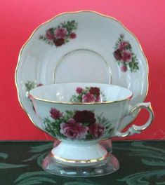 an antique tea cup and saucer with roses on the rim, set against a red background