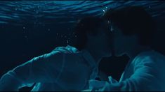 a man and woman kissing under water in the blue light, with bubbles coming from them