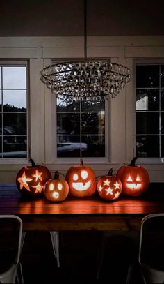 pumpkins with faces carved into them sitting on a wooden table in front of windows