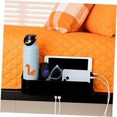 a bed with orange pillows and an electronic device sitting on it's side shelf