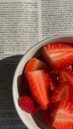 strawberries in a white bowl on top of an open bible book with sunlight shining through the pages