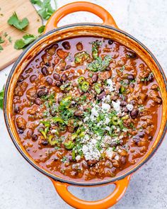 an orange pot filled with chili and beans on top of a white counter next to a cutting board