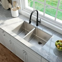 a kitchen sink sitting under a window next to a bowl of fruit on the counter